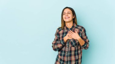 Mavi arka planda izole edilmiş genç bir kadın, dostane bir ifadeye sahip, avuçlarını göğsüne bastırıyor. Aşk konsepti.