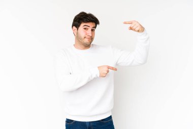 Beyaz arka planda izole edilmiş genç bir adam işaret parmaklarıyla küçük bir şey tutuyor, gülümsüyor ve kendinden emin..