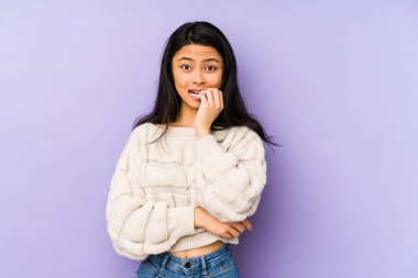 Mor arka planda izole edilmiş, tırnak yiyen, gergin ve endişeli genç Çinli bir kadın..