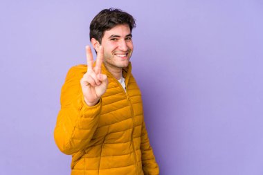 Mor arka planda izole edilmiş genç adam zafer işareti ve geniş bir gülümseme sergiliyor..