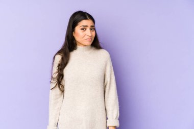 Mor arka planda soyutlanmış genç Hintli kadın omuzlarını silker ve gözleri açık kalır..