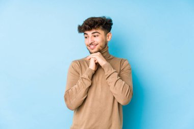 İzole edilmiş genç Arap adam ellerini çenesinin altında tutuyor ve mutlu bir şekilde yan tarafa bakıyor..