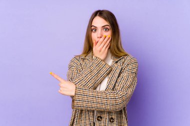Mor arka planda izole edilmiş genç beyaz kadın yan tarafı işaret ediyor.