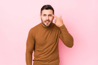 Pembe arka planı olan beyaz bir genç, işaret parmağıyla bir hayal kırıklığı gösteriyor..