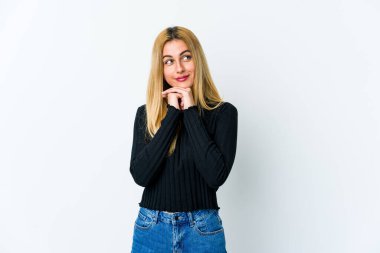 Beyaz arka planda izole edilmiş genç sarışın kadın ellerini çenesinin altında tutuyor ve mutlu bir şekilde yan tarafa bakıyor..