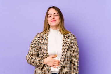 Mor arka planda izole edilmiş genç beyaz kadın karnına dokunuyor, nazikçe gülümsüyor, yemek yiyor ve tatmin oluyor..