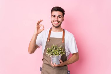 Kafkasyalı genç bahçıvan elinde bir bitki tutuyor neşeli ve kendinden emin..