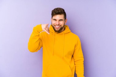 Mor arka planda izole olmuş genç bir adam bir şeye gülüyor, elleriyle ağzını kapatıyor..