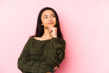 Pembe arka planda izole edilmiş genç Çinli kadın şüpheli ve şüpheci bir ifadeyle yana bakıyor..