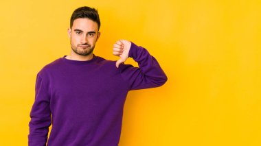 Sarı fırında izole edilmiş genç beyaz adam baş parmağını aşağı gösteriyor, hayal kırıklığı konsepti..