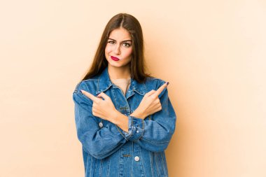 Beyazlı genç bir kadın bej arka planda iki seçenek arasından seçim yapmaya çalışıyor..