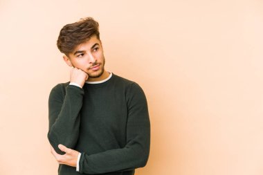 Bej bir arka planda izole edilmiş genç bir Arap adam üzgün ve dalgın hissediyor, kopyalama alanına bakıyor..