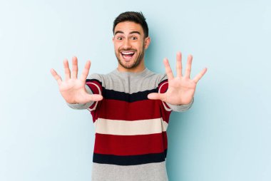 Mavi arka planda izole edilmiş genç beyaz adam on numarayı elleriyle gösteriyor..