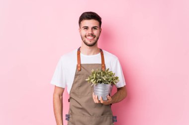 Genç beyaz bahçıvan elinde bir bitki tutuyor mutlu, güler yüzlü ve neşeli..