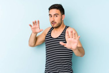 Mavi arka planda izole genç beyaz adam yakın bir tehlike nedeniyle şoka uğruyor