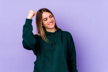 Mor arka planda izole edilmiş genç beyaz kadın zaferi, tutkuyu ve coşkuyu kutluyor, mutlu bir ifade..