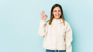 Mavi arka planda izole edilmiş genç bir kadın neşeli ve kendinden emin, iyi bir hareket gösteriyor..