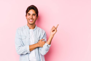 Pembe arka planda poz veren beyaz bir genç yalnız ve neşeli bir şekilde işaret parmağıyla işaret ederek gülümsüyor..