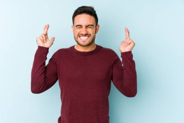 Kafkasyalı genç adam mavi arka planda izole edilmiş şans dilemek için şans diliyor.