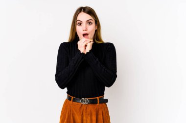 Beyaz arka planda izole edilmiş genç beyaz bir kadın şans için dua ediyor, şaşırmış ve ağzını açıp önüne bakıyor..