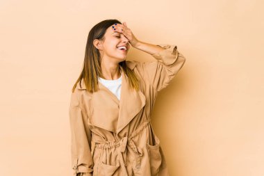 Bej arka planda izole edilmiş genç bir kadın ellerini başının üstünde tutarak neşeyle gülüyor. Mutluluk kavramı.