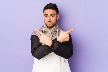 Mor arka plan noktalarında izole genç beyaz adam, iki seçenek arasında seçim yapmaya çalışıyor.