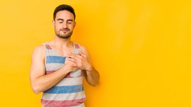 Sarı fırında izole edilmiş beyaz bir genç, dost bir ifadeye sahip, avuçlarını göğsüne bastırıyor. Aşk konsepti.