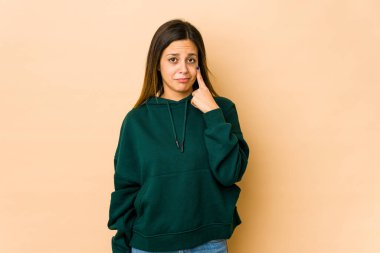 Bej arka planda izole edilmiş genç bir kadın ağlıyor, bir şeyden memnun değil, acı ve kafa karışıklığı konsepti..