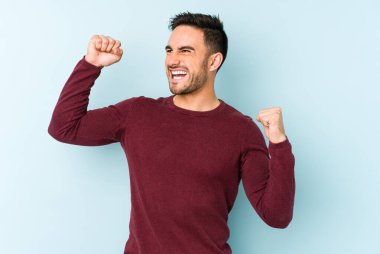 Mavi arka planda izole edilmiş genç beyaz bir adam zaferden sonra yumruğunu kaldırıyor, kazanan konsept..