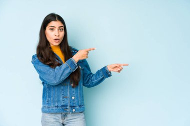 Mavi arka planda izole edilmiş genç Hintli kadın işaret parmaklarıyla fotokopi alanını işaret ederek heyecan ve arzusunu ifade ediyor..