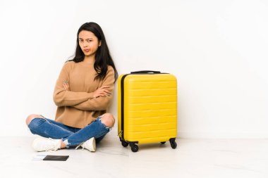 Genç Çinli gezgin bir bavulla yerde oturuyor hoşnutsuzca kaşlarını çatmış, kollarını kavuşturmuş..