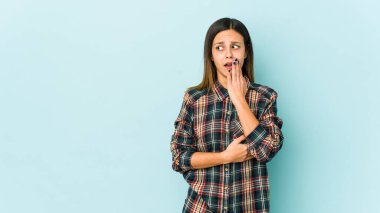Mavi arka planda izole edilmiş genç bir kadın esniyor. Ağzı eliyle kapatan yorgun bir jest gösteriyor..