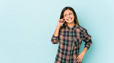 Mavi arka planda izole edilmiş genç bir kadın kulakları elleriyle kapatıyor..