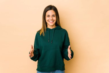 Bej arka planda izole edilmiş genç bir kadın iki eliyle bir şey tutuyor, ürün sunumu.