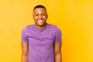 Sarı arka planda izole edilmiş genç latin adam gülüyor ve gözlerini kapıyor, rahatlamış ve mutlu hissediyor..