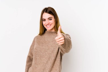 Beyaz arka planda izole edilmiş genç beyaz kadın gülümsüyor ve başparmağını kaldırıyor.