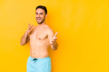 Sarı arka planda mayosu olan genç, beyaz bir adam..... kameraya sarılıyor..