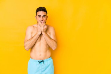 Sarı arka planda mayosu olan genç, beyaz bir adam. Ağzı açık ve endişeli görünen beyaz bir adam..