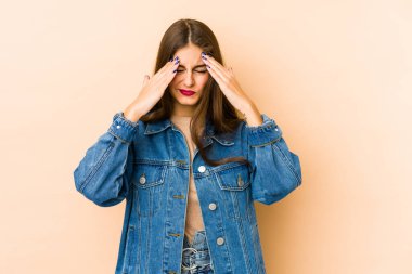 Kafkasyalı genç bir kadın bej arka planda izole edilmiş, başı ağrıyor, yüzüne dokunuyor..