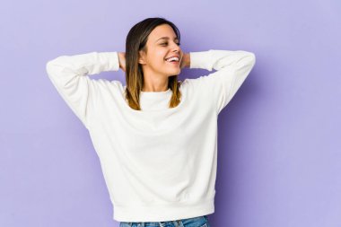 Mor arka planda izole edilmiş genç bir kadın kendini güvende hissediyor, elleri başının arkasında..