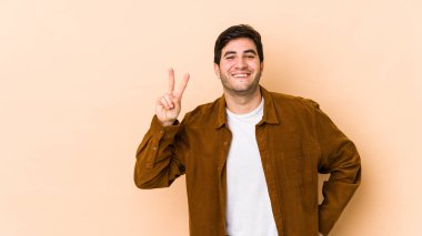 Bej arka planda izole edilmiş genç bir adam iki numarayı parmaklarıyla gösteriyor..