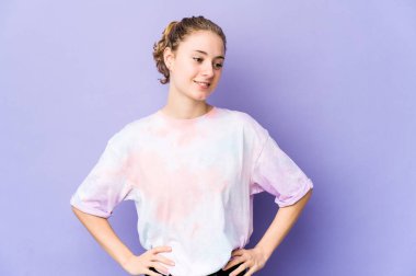 Mor arka planda genç beyaz bir kadın ellerini kalçasından ayırmıyor..