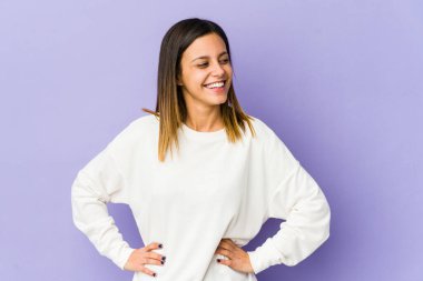 Mor arka planda izole edilmiş genç bir kadın. Kendine güveniyor. Ellerini kalçasında tutuyor..
