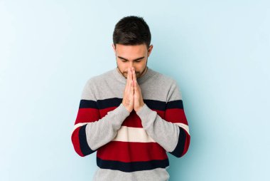 Kafkasyalı genç adam mavi arka planda izole edilmiş dua ediyor, bağlılık gösteriyor, dindar biri ilahi ilham arıyor..