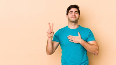 Genç adam bej arka planda izole edilmiş. Yemin ediyor, elini göğsüne koyuyor..