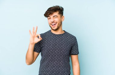 Mavi arka planda izole edilmiş genç bir Arap göz açıp kapayıncaya kadar iyi bir el hareketi yapar..