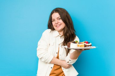 Genç kıvrımlı kadın elinde tatlı pastalarla gülüyor ve eğleniyor..