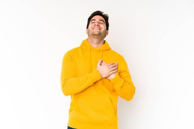 Beyaz arka planda yalnız yaşayan genç adam gülüyor, elleri kalbinde, mutluluk kavramında..