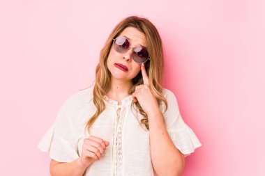 Pembe arka planda gözlüklü genç beyaz kadın ağlıyor, bir şeyden mutsuz, acı ve kafa karışıklığı konsepti..