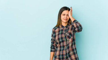 Mavi arka planda izole edilmiş genç bir kadın yorgun ve uykulu. Elini başının üstünde tutuyor..